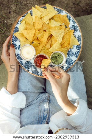A person eat crunchy nachos with guacamole, tomatoes and cheese sauce. Mexican food