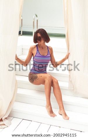 Beautiful woman in swimsuit at backyard pool at summer sunny day enjoying amazing warm weather, catching sun rays