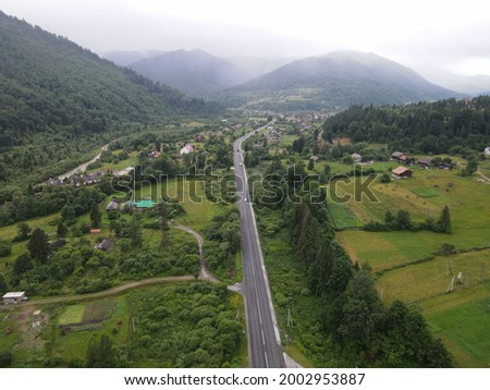 Road through typical Carpathians village of Korostiv in Lviv region, Ukraine, on rainy summer morning, aerial view. Beauty of Ukrainian nature. Walking route to the mountains. Weather changes. 