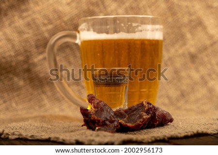 Pieces of dried caviar, a glass of vodka and a mug of beer on a table covered with a homespun cloth with a rough texture. Close-up, selective focus.