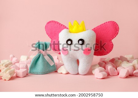 Cute toy for Tooth Fairy Day as funny smiling cartoon character of tooth fairy with crown, wings on pink background, copy space flyer, concept children milk toothless, funny toy, handmade felt diy