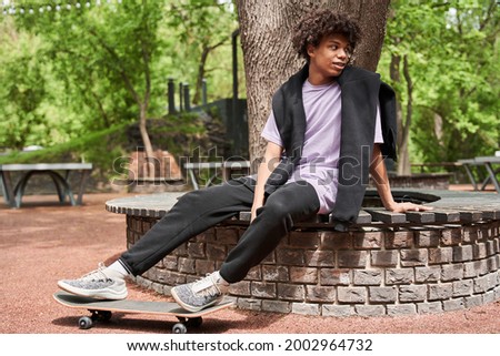 Skateboarder sitting at the bench and looking away while enjoying