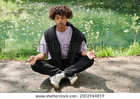 Calm man keeping eyes closed and meditating at the cozy forest or park
