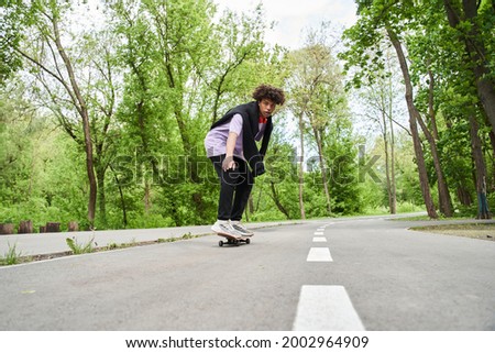 Man with curly hair performing with skateboard on a road at the summer street