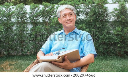 Asian senior men relax at home. Asian Senior Chinese male enjoy rest time wear glasses read books while lying in the garden at home in the morning concept. Royalty-Free Stock Photo #2002974566