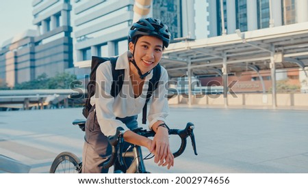 Asian businesswoman go to work at office stand and smiling wear backpack look at camera with bicycle on street around building on a city. Bike commuting, Commute on bike, Business commuter concept. Royalty-Free Stock Photo #2002974656