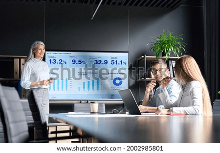 Middle aged happy successful Asian business woman ceo executive manager presenting to colleagues trainees interns income revenue financial data research results on big screen in modern office.