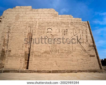 Wall Reliefs on The right side of the first pylon at Habu Temple showing Ramesses III wearing the red crown smites his prisoners in Luxor . Egypt.