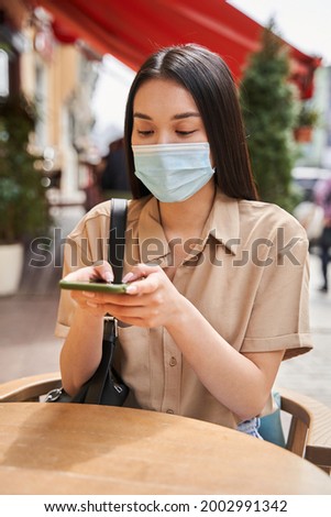 Woman sitting at the table at the cafe and holding smartphone before the making order