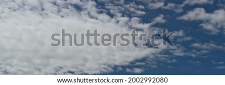 Blue summer sky covered with white clouds. Fluffy white clouds float across the sky on a clear day with warm sunlight