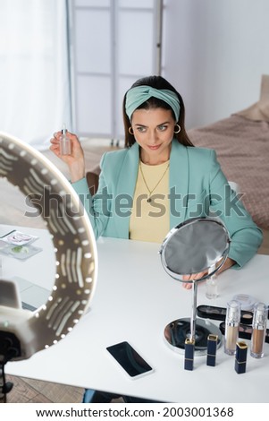 beauty blogger holding bottle of face serum near phone holder with ring lamp