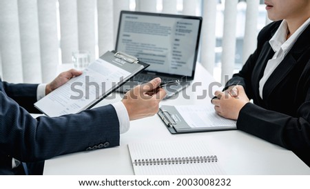 Man employer in suit is holding resume of applicant to reading her profile and asking candidate question while sitting to job interview and explaining about job description in office Royalty-Free Stock Photo #2003008232