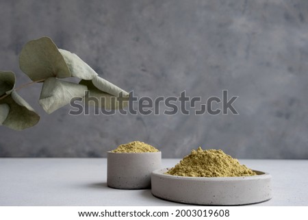 .henna powder for dyeing hair and eyebrows and drawing mehendi on hands on a gray cement pedestal with dried flowers or a white flower.