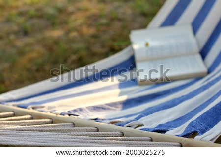 striped hammock with a blurred silhouette of a book on it. time to relax in the garden