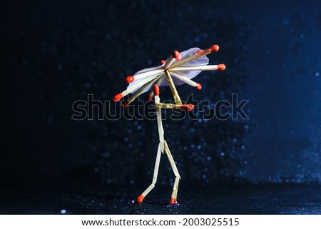 A matchstick man with a matchstick umbrella in the rain. Raining concept. Matchstick art photography used matchsticks to create the character. Royalty-Free Stock Photo #2003025515