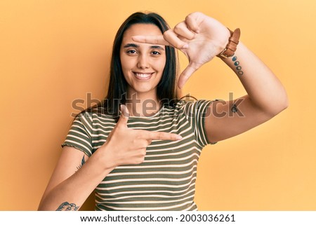 Young hispanic woman wearing casual striped t shirt smiling making frame with hands and fingers with happy face. creativity and photography concept. 