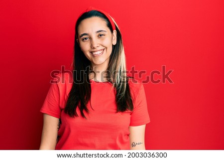 Young hispanic woman wearing casual red t shirt with a happy and cool smile on face. lucky person. 
