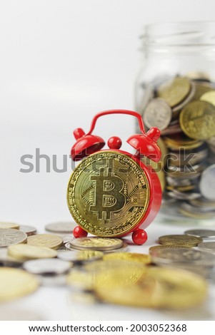 Selective focus of Bitcoin and alarm clock. Deadline to invest in cryptocurrency concept. New financial asset. Decentralized bitcoin network. Purchasing power of money. Photo contains noise and grain.