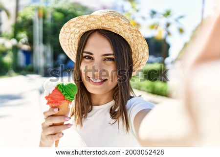 Young beautiful woman smiling happy outdoors on a sunny day wearing a summer hat and eating ice cream taking a selfie picture