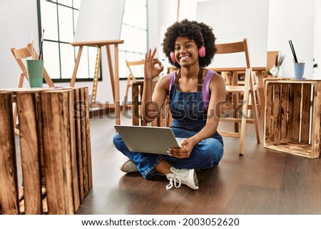 Young african american woman with afro hair at art studio using laptop doing ok sign with fingers, smiling friendly gesturing excellent symbol 