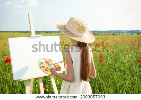 Little girl painting on easel in beautiful poppy field