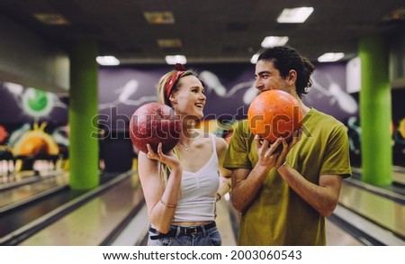 Cheerful young couple at the bowling alley with the balls looking at each other. Young man and woman standing in a bowling club holding balls.