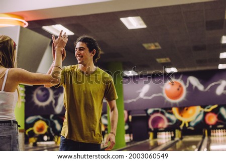 Friends celebrating bowling strike with high five. Cheerful young man and woman looking at each other and giving high five after strike at bowling alley.