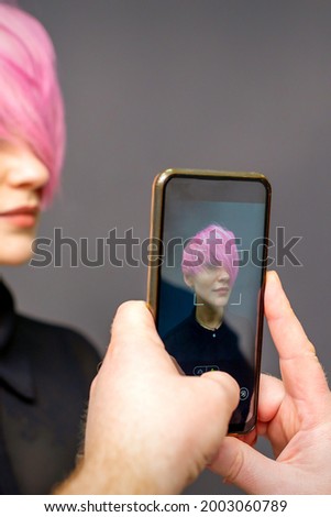 Man hairdresser's hands taking picture on smartphone of her client short pink hairstyle