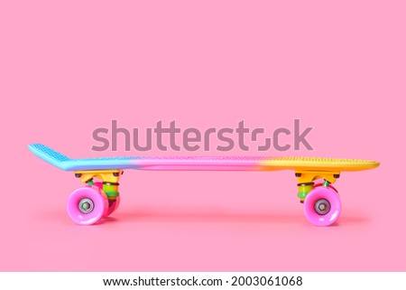 Pastel neon rainbow colored Penny board skateboard isolated on solid soft pink background. Plastic mini cruiser. Youth minimalistic Sport inspired summer fun concept. Copy space.