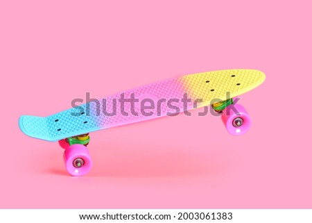 Pastel neon rainbow colored Penny board skateboard standing on two wheels isolated on solid soft pink background. Plastic mini cruiser Youth minimalistic Sport inspired summer fun concept. Copy space.