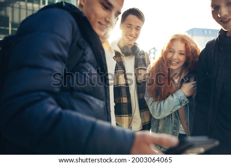 Students enjoying watching something on mobile phone. Young man showing his cell phone to his friends in college campus.