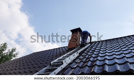 a man climbs a metal ladder to the roof of the bathhouse to clean the pipe from soot and soot Royalty-Free Stock Photo #2003066195