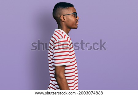 Young african american man wearing casual t shirt and glasses looking to side, relax profile pose with natural face with confident smile. 