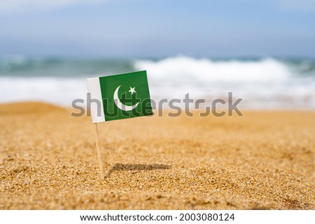 Flag of Pakistan in the form of a toothpick in the sand of beach opposite sea wave. Travel concept