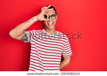 Young african american guy wearing casual clothes and glasses smiling happy doing ok sign with hand on eye looking through fingers 