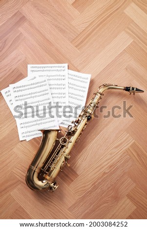 Beautiful saxophone and note sheets on wooden background, flat lay