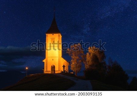 Scenic view of illuminated Jamnik church St Primus and Felician on the hill at night, Slovenia. Beautiful landscape with blue starry sky, outdoor travel background, famous tourist attraction