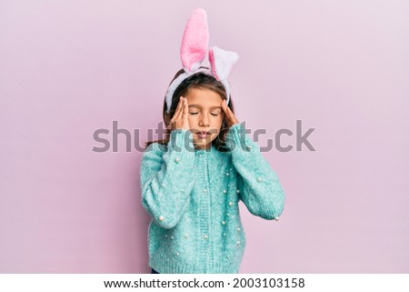 Little beautiful girl wearing cute easter bunny ears with hand on head for pain in head because stress. suffering migraine. 