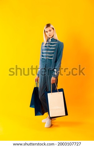 
Pretty girl in royal army outfit carrying shopping bags standin. gBlonde hair girl posing with shopping paper bags. Shopping and presenting concept. Photo for fashion, beauty, art and advertising 