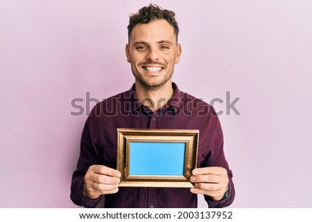 Young hispanic man holding empty frame smiling with a happy and cool smile on face. showing teeth. 