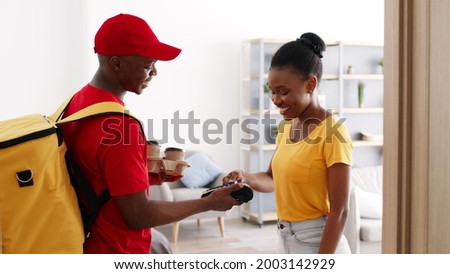 Coffee shop delivery. Young cheerful african american woman paying for order with credit card and getting coffee-to-go from courier in morning at home, slow motion