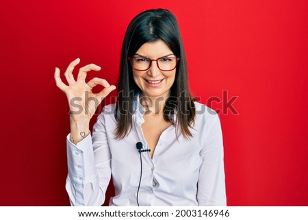 Young hispanic woman using lavalier microphone doing ok sign with fingers, smiling friendly gesturing excellent symbol 
