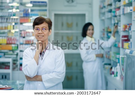 female pharmacist standing back couunter with hand on chin in pharmacy Thailand 

