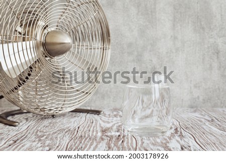 Transparent glass of clear water and a small table fan on a wooden table closeup, shallow depth of field