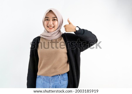 Beautiful asian muslim woman smiling confident and happy with finger on left hand showing thumbs up isolated on white background, advertising concept