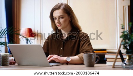 Brunette woman wearing casual clothes working on internet. Woman is looking to the camera and using laptop computer. Picture showing pretty woman working and rejoicing