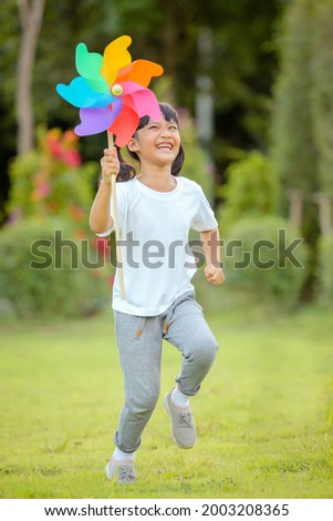 Cute little girl playing on the colorful toy windmill  in her hands at the lawn. Which increases the development and enhances learning skills renewable energies and sustainable resources.