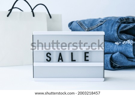 Light board with text SALE with paper shopping bags, jeans clothes. Big Sale online shopping concept. Promotion advertising. Holiday Cyber monday.