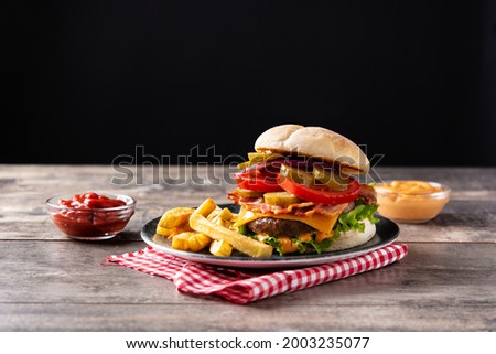 Beef burger with cheese, bacon and french fries on wooden table