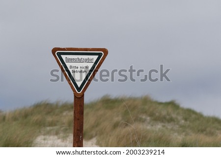 A triangle sign: Dune protection area, please do not enter with dunes and grass in the background 